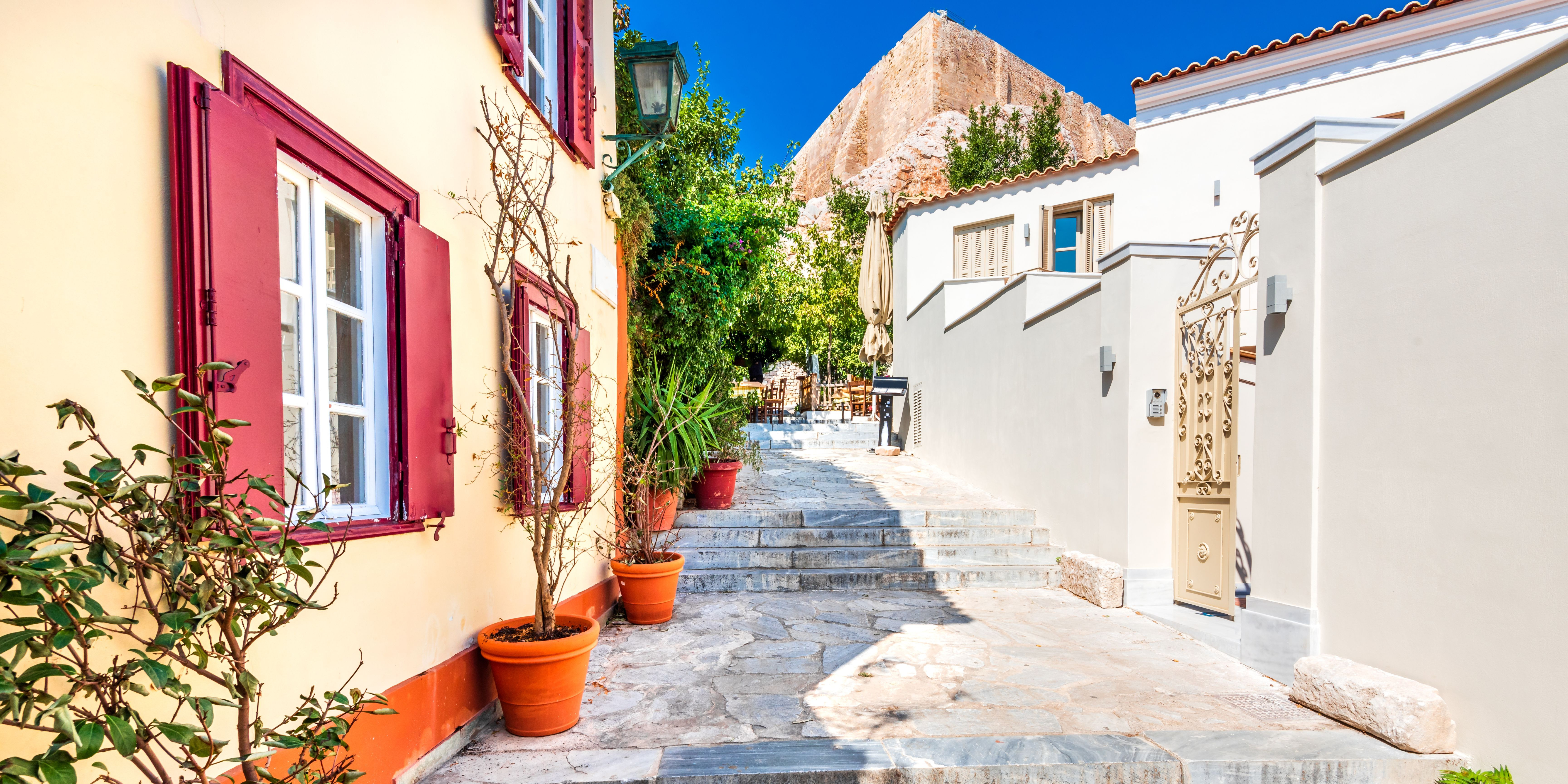 A stone-paved alley in the Plaka neighborhood with colorful houses and potted plants.